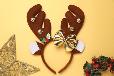 Photo of Beautiful reindeer headband and Christmas decor on pale yellow background, flat lay