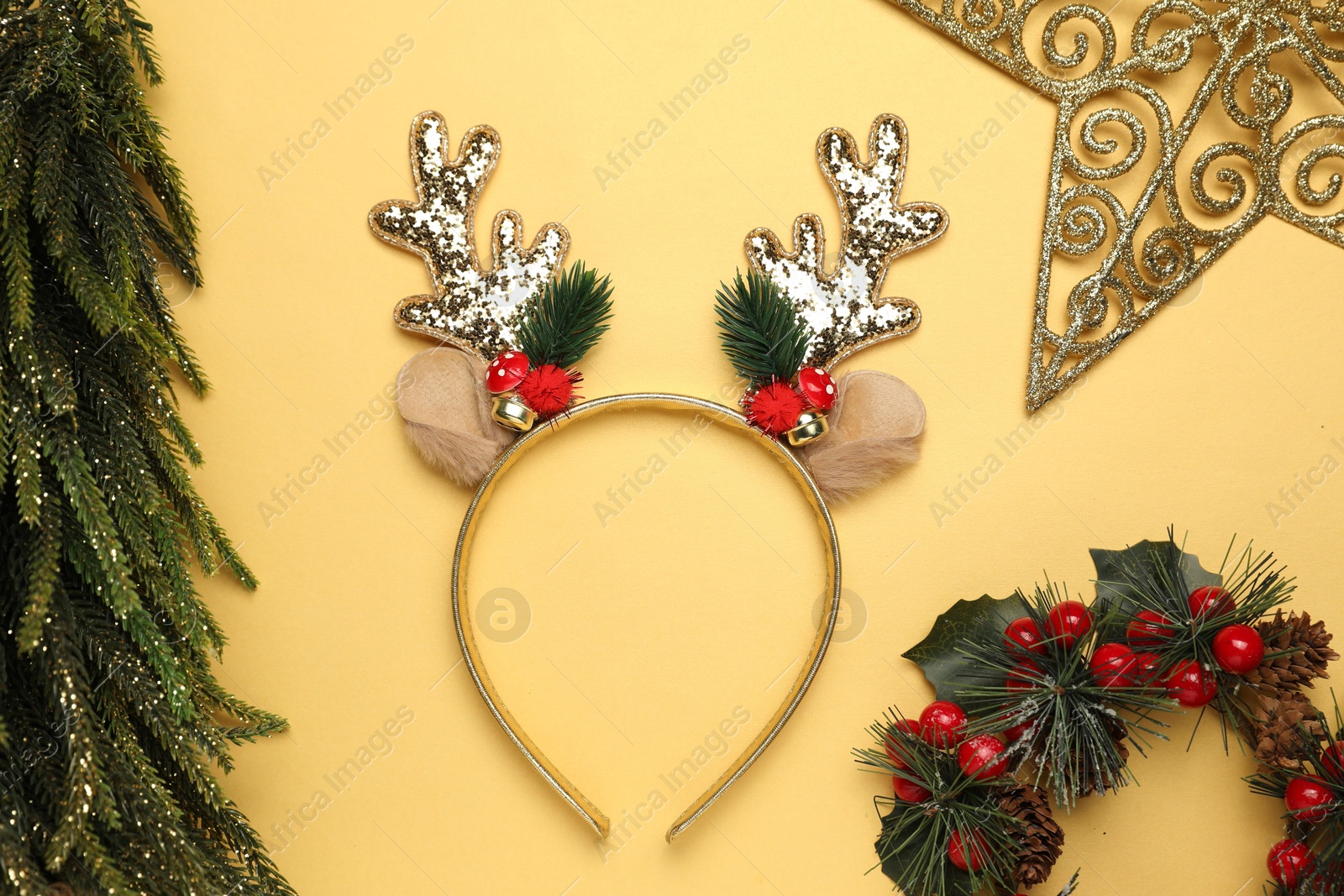 Photo of Beautiful reindeer headband and Christmas decor on pale yellow background, flat lay