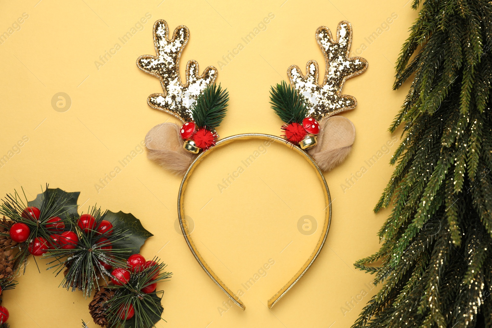 Photo of Beautiful reindeer headband and Christmas decor on pale yellow background, flat lay