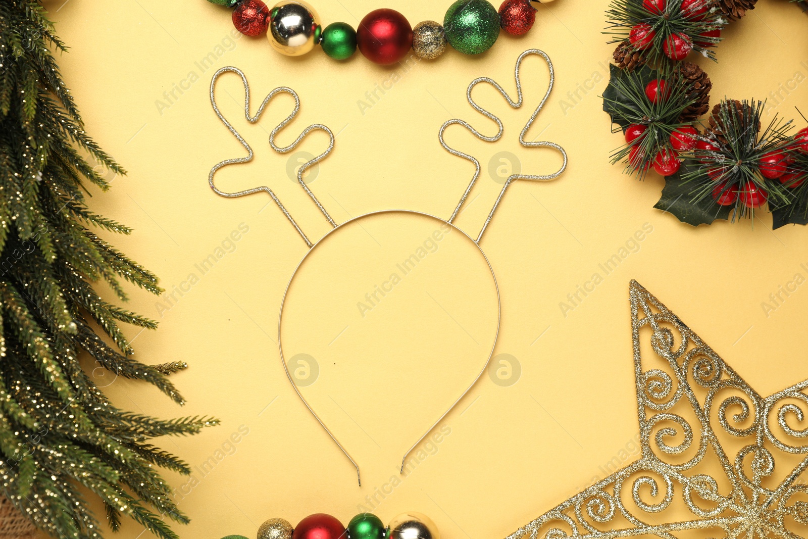 Photo of Beautiful reindeer headband and Christmas decor on pale yellow background, flat lay