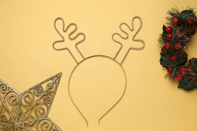 Photo of Beautiful reindeer headband and Christmas decor on pale yellow background, flat lay