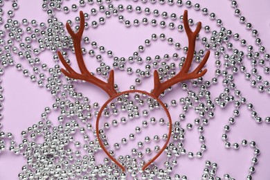 Photo of Beautiful reindeer headband and Christmas beads on lilac background, top view