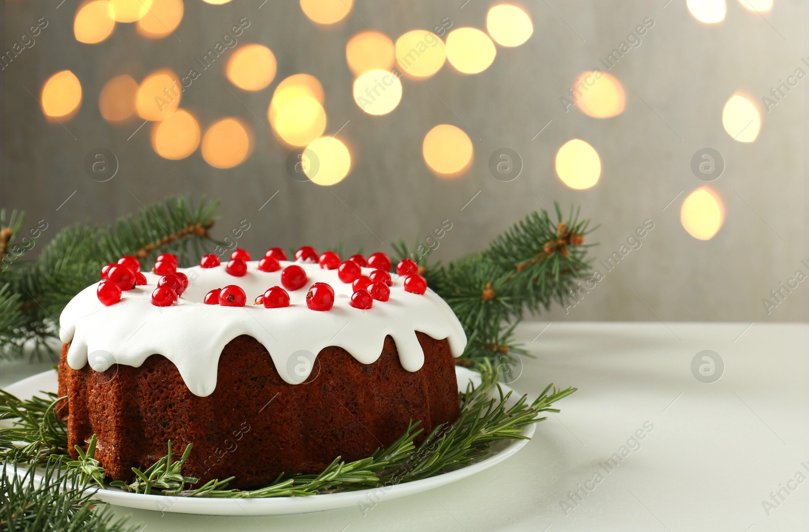 Photo of Traditional classic Christmas cake and fir branches on white table against blurred lights. Space for text