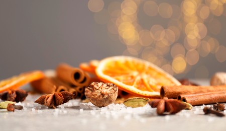 Photo of Different spices and dried orange slices on light grey table, closeup. Christmas season