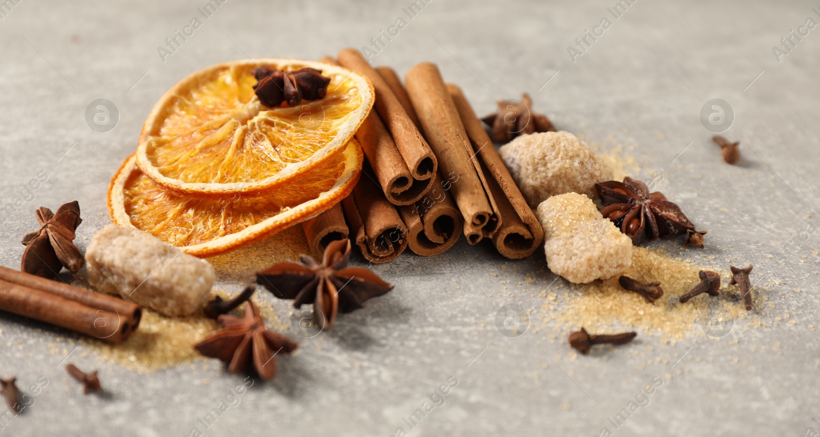 Photo of Different spices and dried orange slices on light grey table, closeup. Christmas season