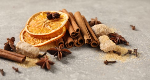 Photo of Different spices and dried orange slices on light grey table, closeup. Christmas season