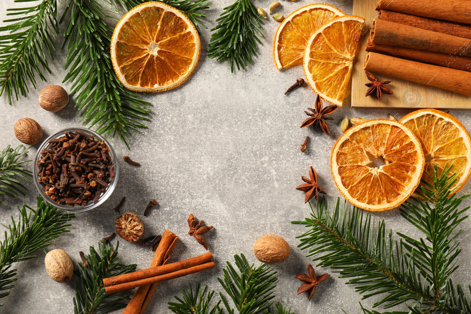 Photo of Different spices, dried orange slices and fir tree branches on light grey table, flat lay with space for text. Christmas season