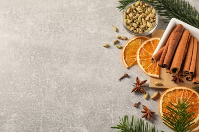 Photo of Different spices, dried orange slices and fir tree branches on light grey table, flat lay with space for text. Christmas season