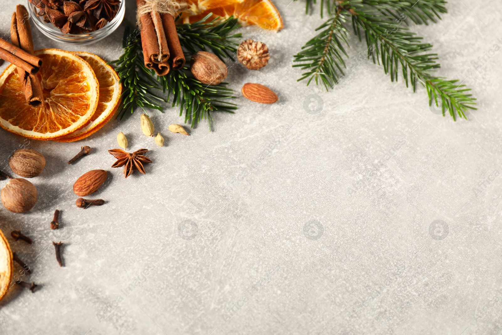 Photo of Different spices, dried orange slices and fir tree branches on light grey table, above view with space for text. Christmas season