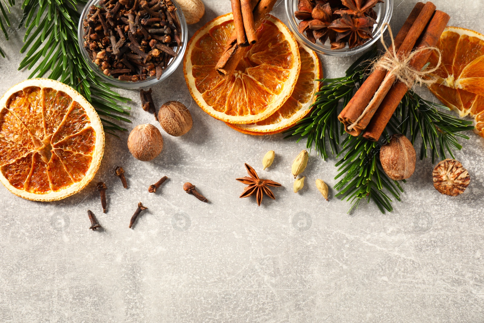 Photo of Different spices, dried orange slices and fir tree branches on light grey table, flat lay. Christmas season