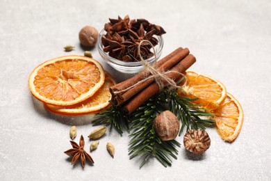 Photo of Different spices, dried orange slices and fir tree branches on light grey table. Christmas season