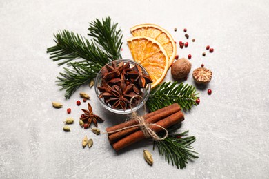 Photo of Different spices, dried orange slices and fir tree branches on light grey table. Christmas season