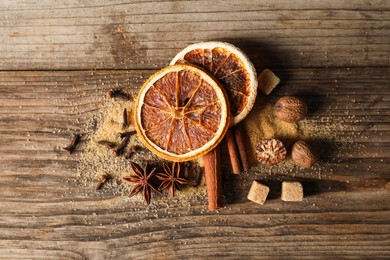 Photo of Different spices and dried orange slices on wooden table, flat lay. Christmas season