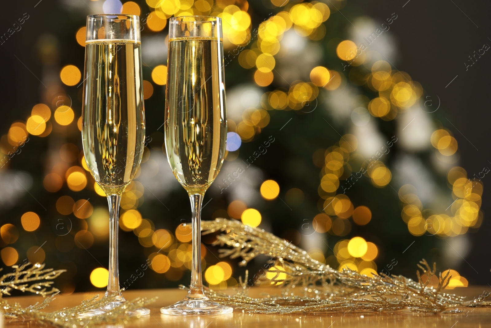 Photo of Champagne in glasses and decor on table against blurred Christmas lights, space for text. Bokeh effect