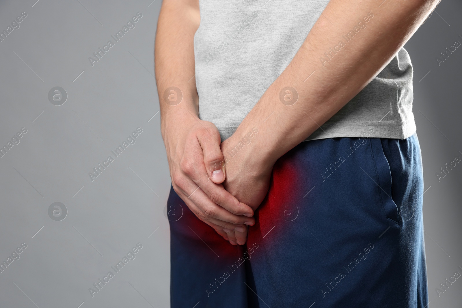 Image of STD (sexually transmitted diseases). Man holding hands near his groin on grey background, closeup. Space for text