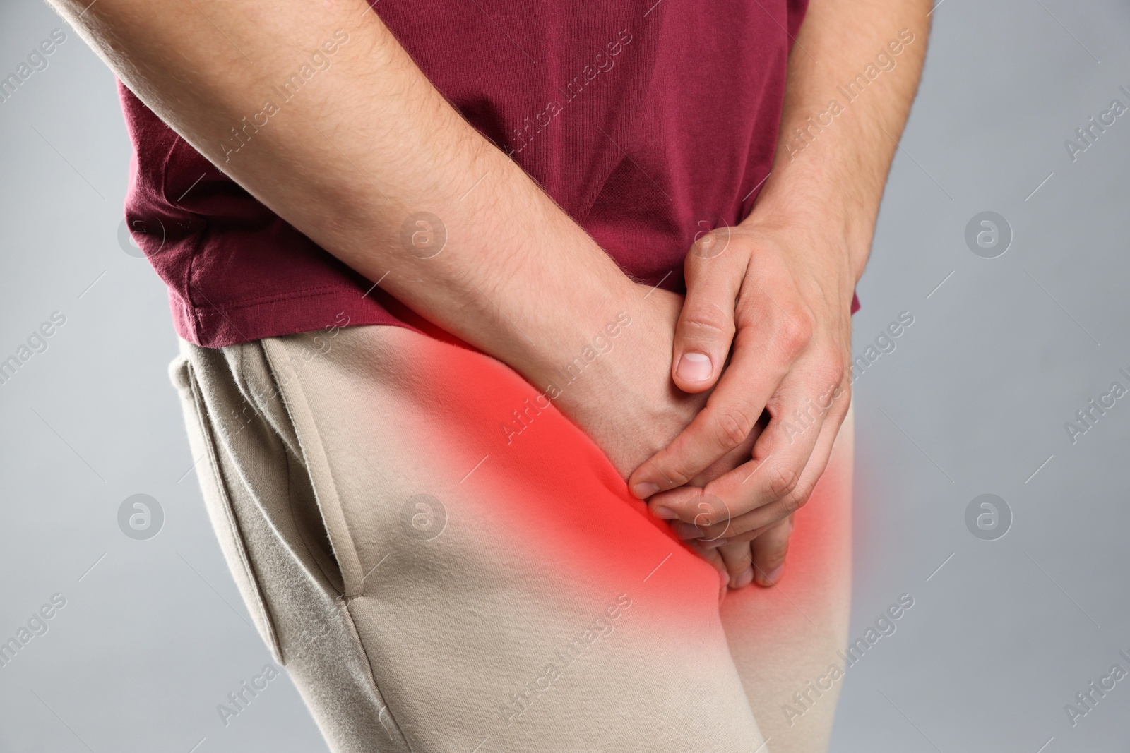 Image of STD (sexually transmitted diseases). Man holding hands near his groin on grey background, closeup