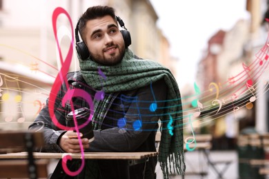 Image of Smiling man with headphones and paper cup in outdoor cafe. Music notes flying near him