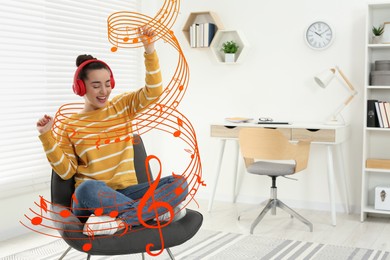 Image of Happy woman with headphones dancing on cosy armchair at home. Music notes flying near her