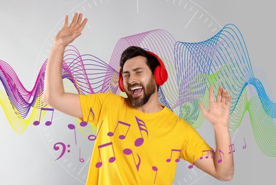 Image of Happy man with headphones dancing on light grey background. Music notes and sound waves near him