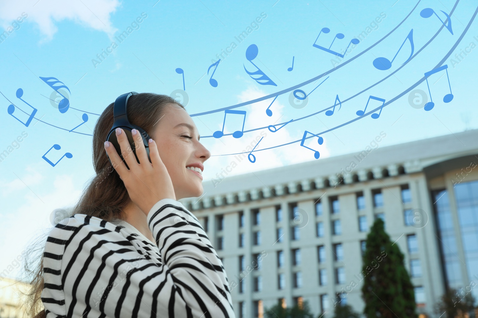 Image of Happy woman with headphones on city street. Music notes flying near her