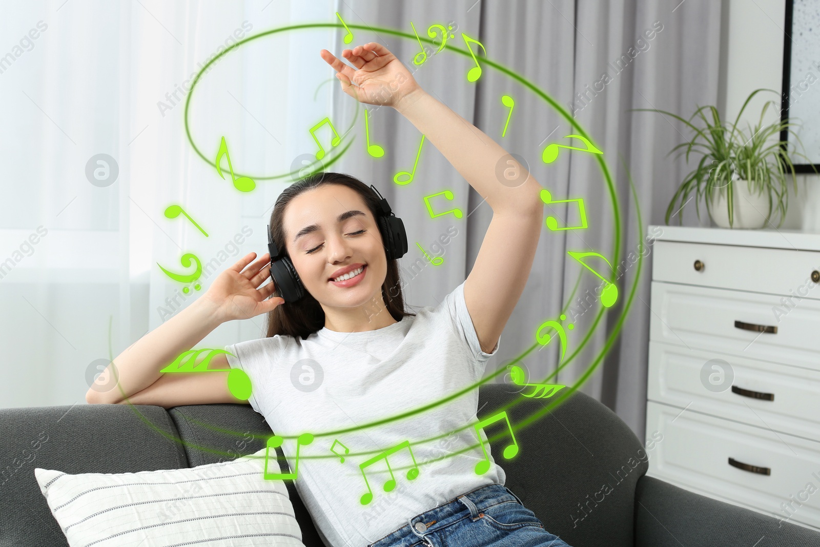 Image of Happy woman with headphones dancing on sofa at home. Music notes flying near her