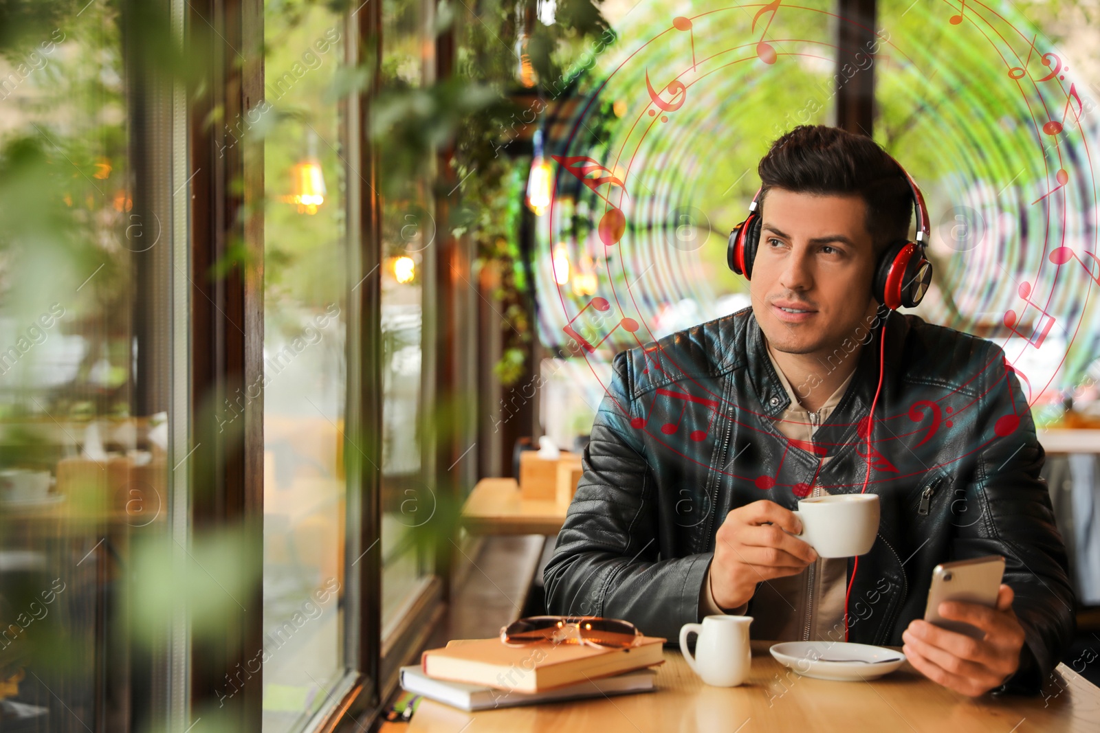 Image of Man with headphones drinking coffee at table in cafe. Music notes flying near him