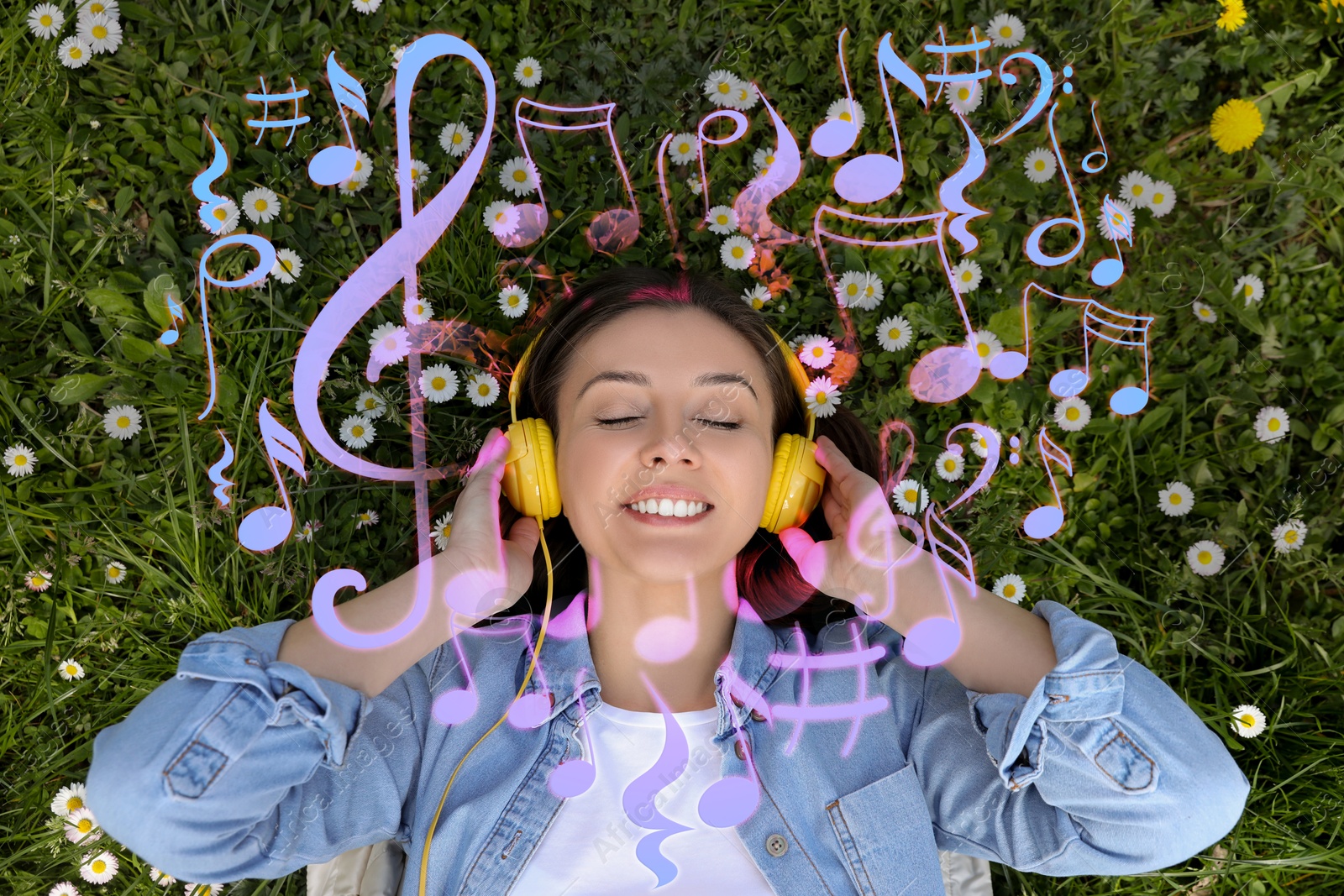 Image of Happy woman with headphones lying on green grass, top view. Heart of music notes around near her