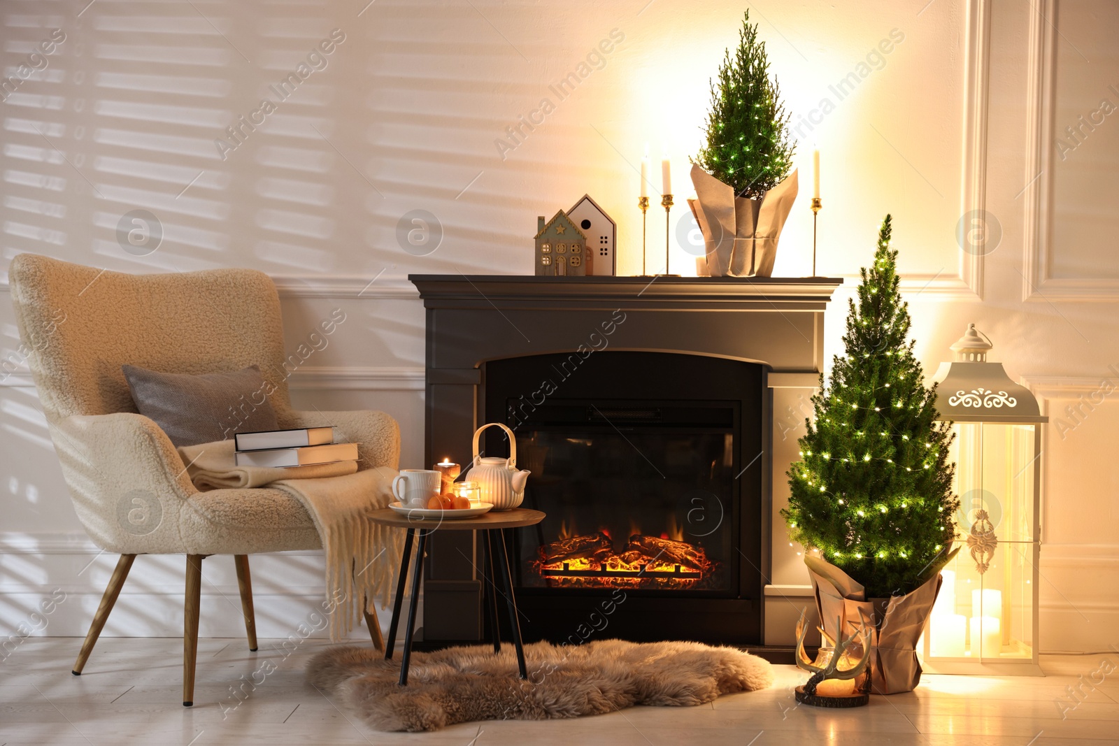 Photo of Small spruce trees decorated with Christmas lights near fireplace indoors