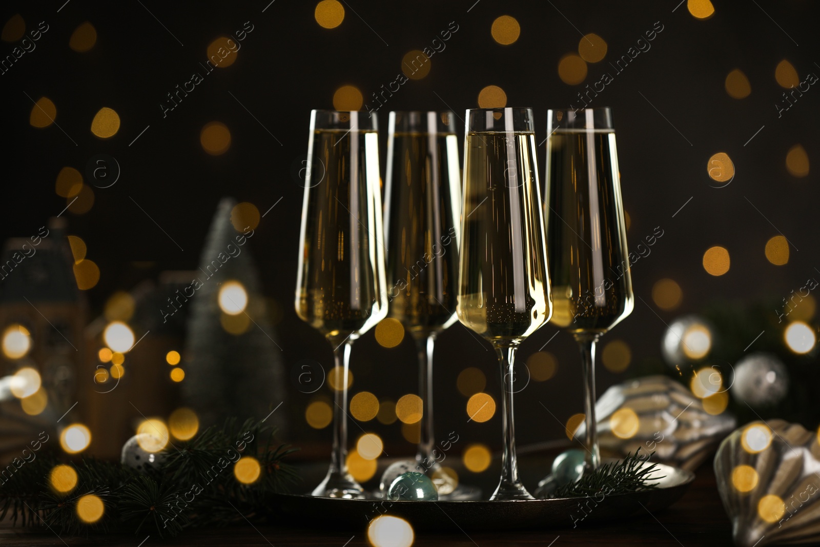 Photo of Champagne in glasses and decor on wooden table against blurred Christmas lights. Bokeh effect