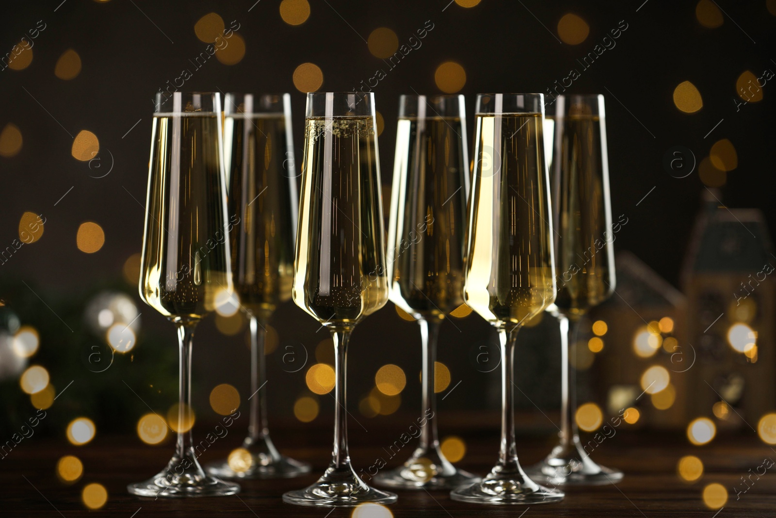 Photo of Champagne in glasses and decor on wooden table against blurred Christmas lights. Bokeh effect