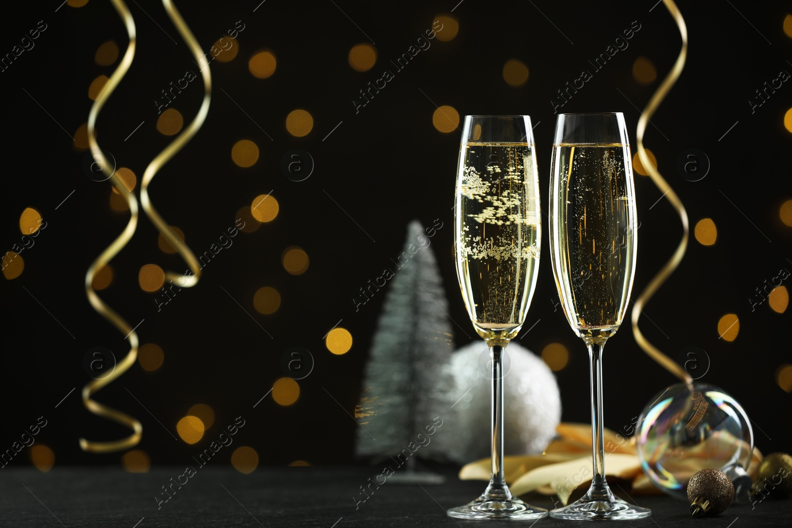 Photo of Delicious champagne in glasses and Christmas decor on black table against blurred lights, space for text