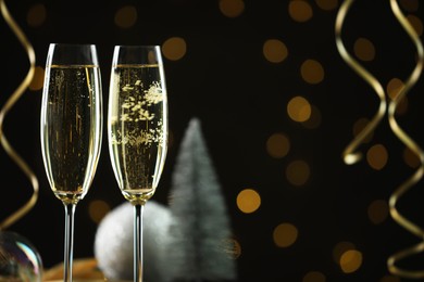 Photo of Delicious champagne in glasses and Christmas decor against black background with blurred lights, closeup. Space for text