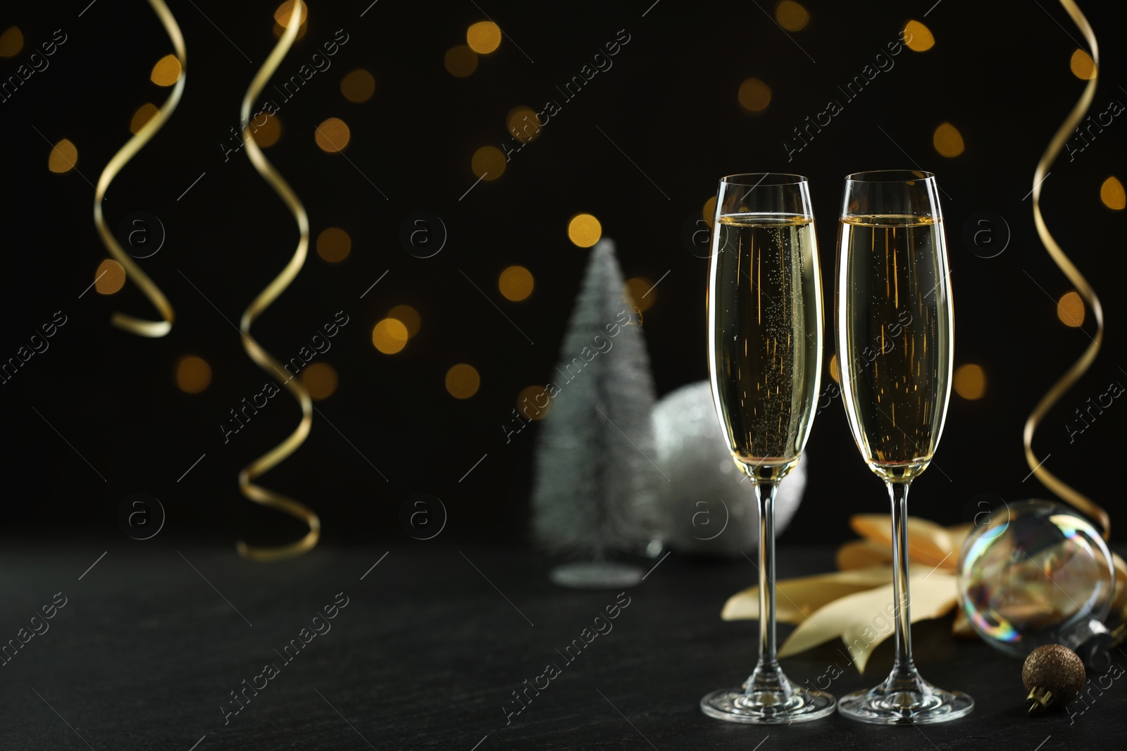 Photo of Delicious champagne in glasses and Christmas decor on black table against blurred lights, space for text