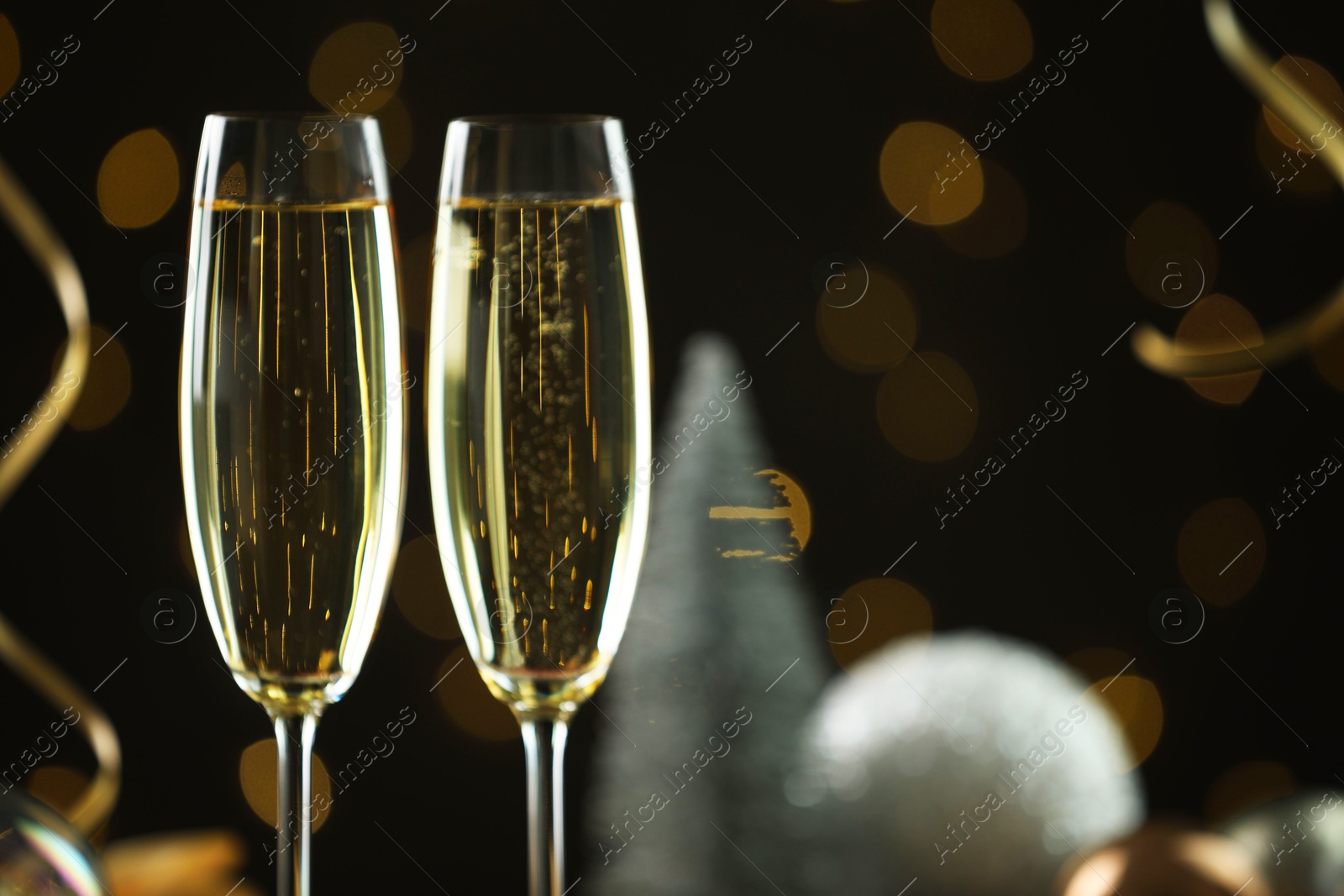 Photo of Delicious champagne in glasses and Christmas decor against black background with blurred lights, closeup. Space for text