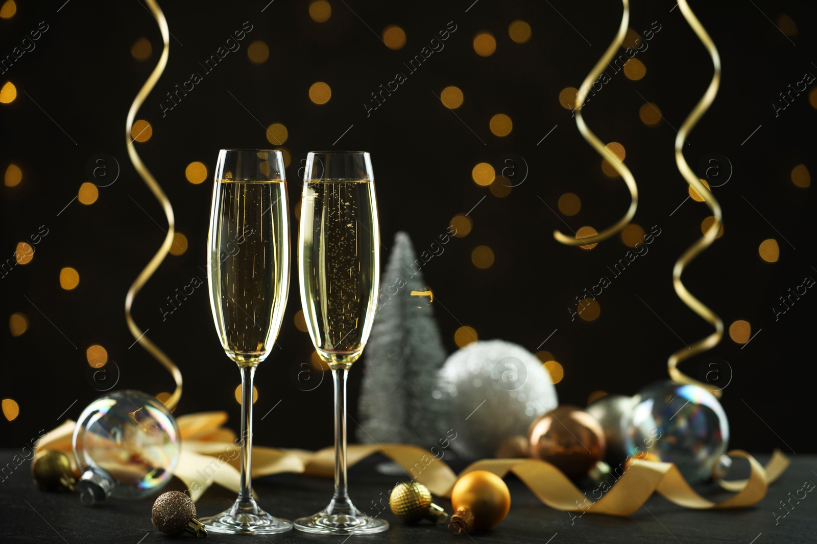 Photo of Delicious champagne in glasses and Christmas decor on black table against blurred lights, space for text