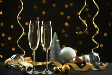 Photo of Delicious champagne in glasses and Christmas decor on black table against blurred lights, space for text