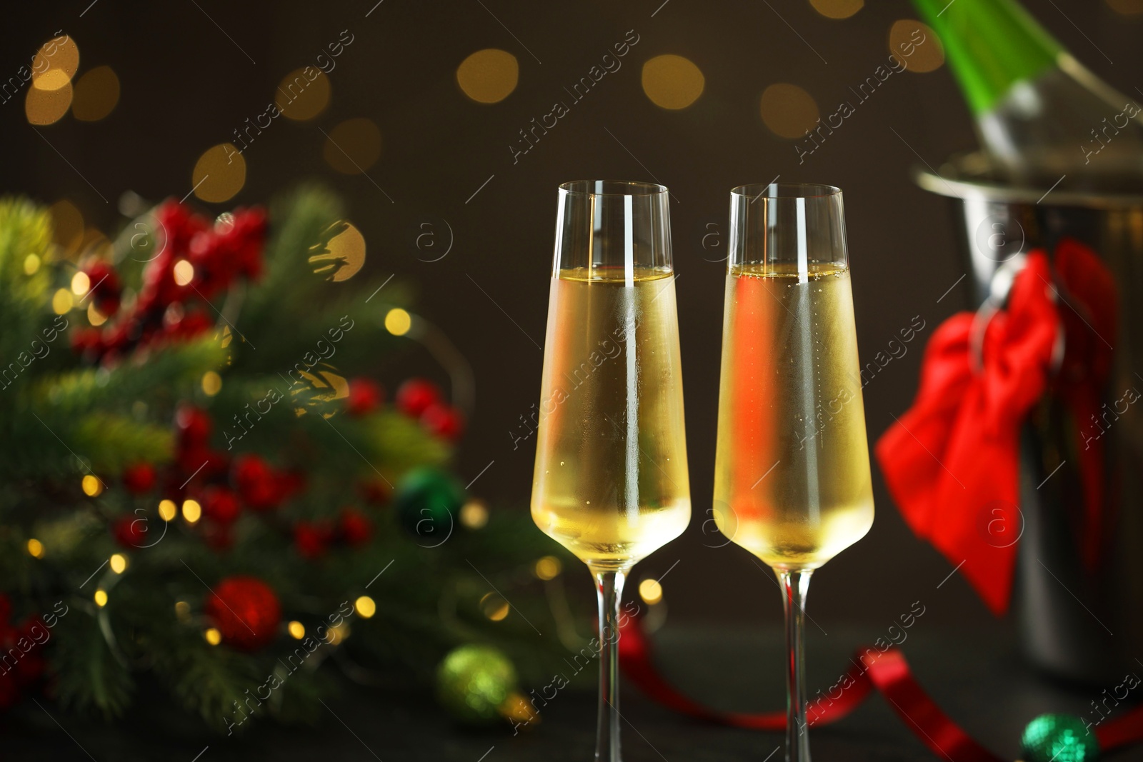 Photo of Delicious champagne in glasses and Christmas decor against grey background with blurred lights, closeup. Space for text