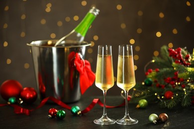 Photo of Delicious champagne in glasses and Christmas decor on grey table against blurred lights