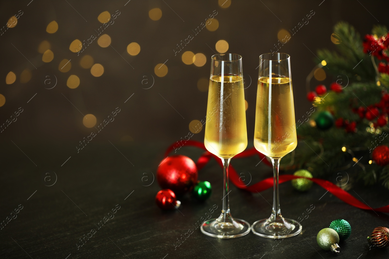 Photo of Delicious champagne in glasses and Christmas decor on grey table against blurred lights, space for text