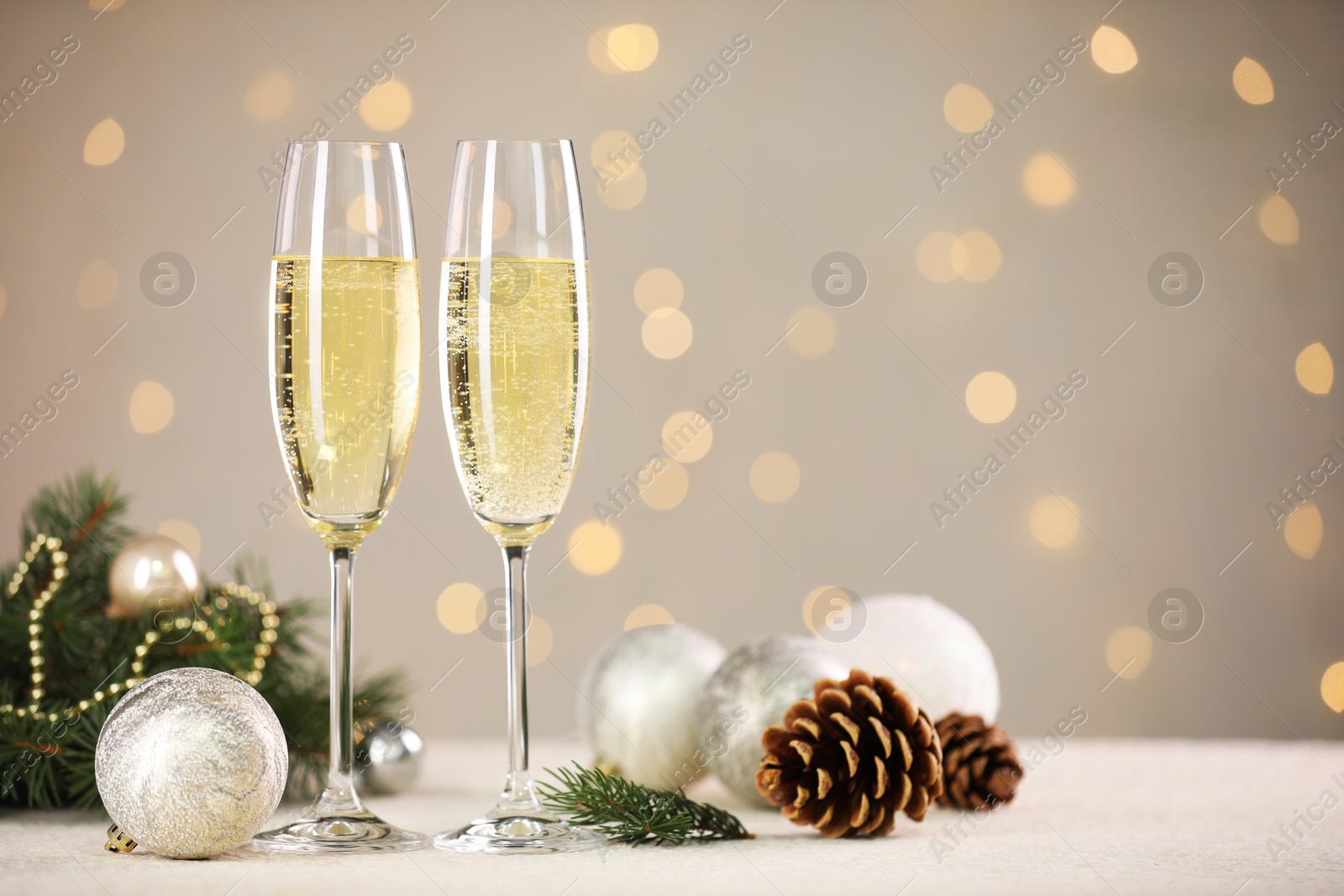 Photo of Delicious champagne in glasses and Christmas decor on white table against blurred lights, space for text