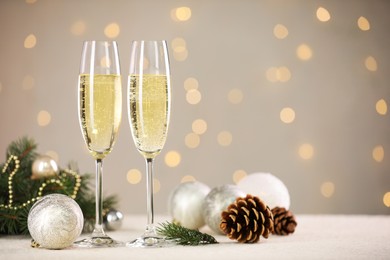 Photo of Delicious champagne in glasses and Christmas decor on white table against blurred lights, space for text