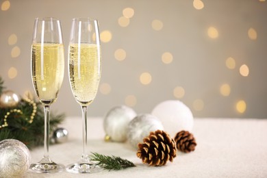 Photo of Delicious champagne in glasses and Christmas decor on white table against blurred lights, space for text