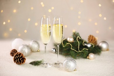 Photo of Delicious champagne in glasses and Christmas decor on white table against blurred lights