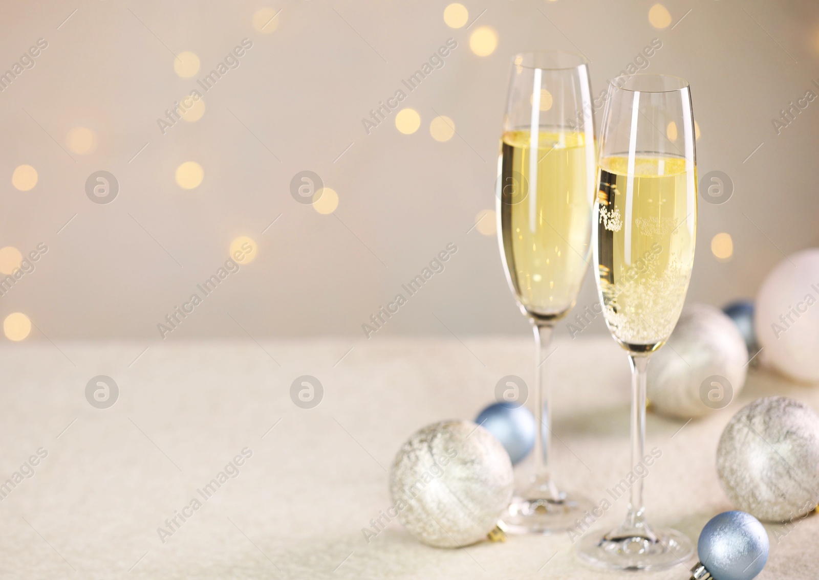 Photo of Delicious champagne in glasses and Christmas decor on white table against blurred lights, space for text