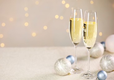 Photo of Delicious champagne in glasses and Christmas decor on white table against blurred lights, space for text