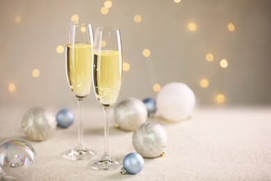 Photo of Delicious champagne in glasses and Christmas decor on white table against blurred lights, space for text