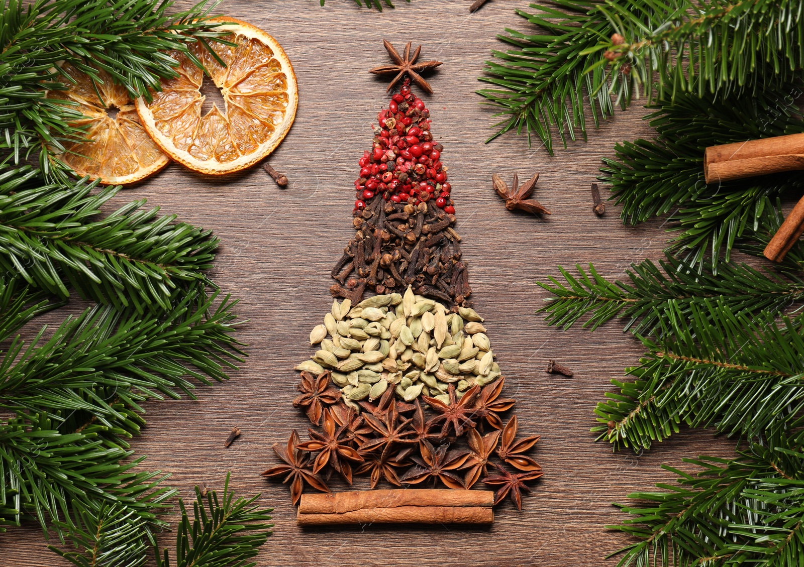 Photo of Christmas tree made of different spices, dried orange slices and fir branches on wooden table, flat lay