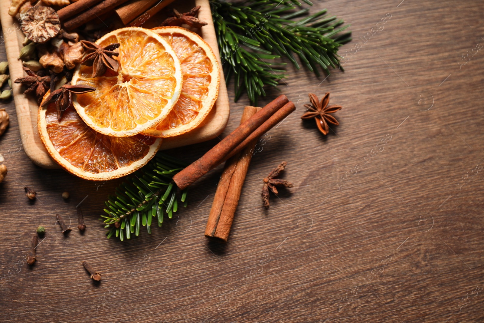 Photo of Different spices, dried orange slices and fir tree branches on wooden table, flat lay with space for text. Christmas season