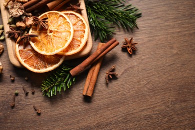 Photo of Different spices, dried orange slices and fir tree branches on wooden table, flat lay with space for text. Christmas season