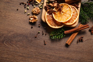 Photo of Different spices, dried orange slices and fir tree branches on wooden table, flat lay with space for text. Christmas season